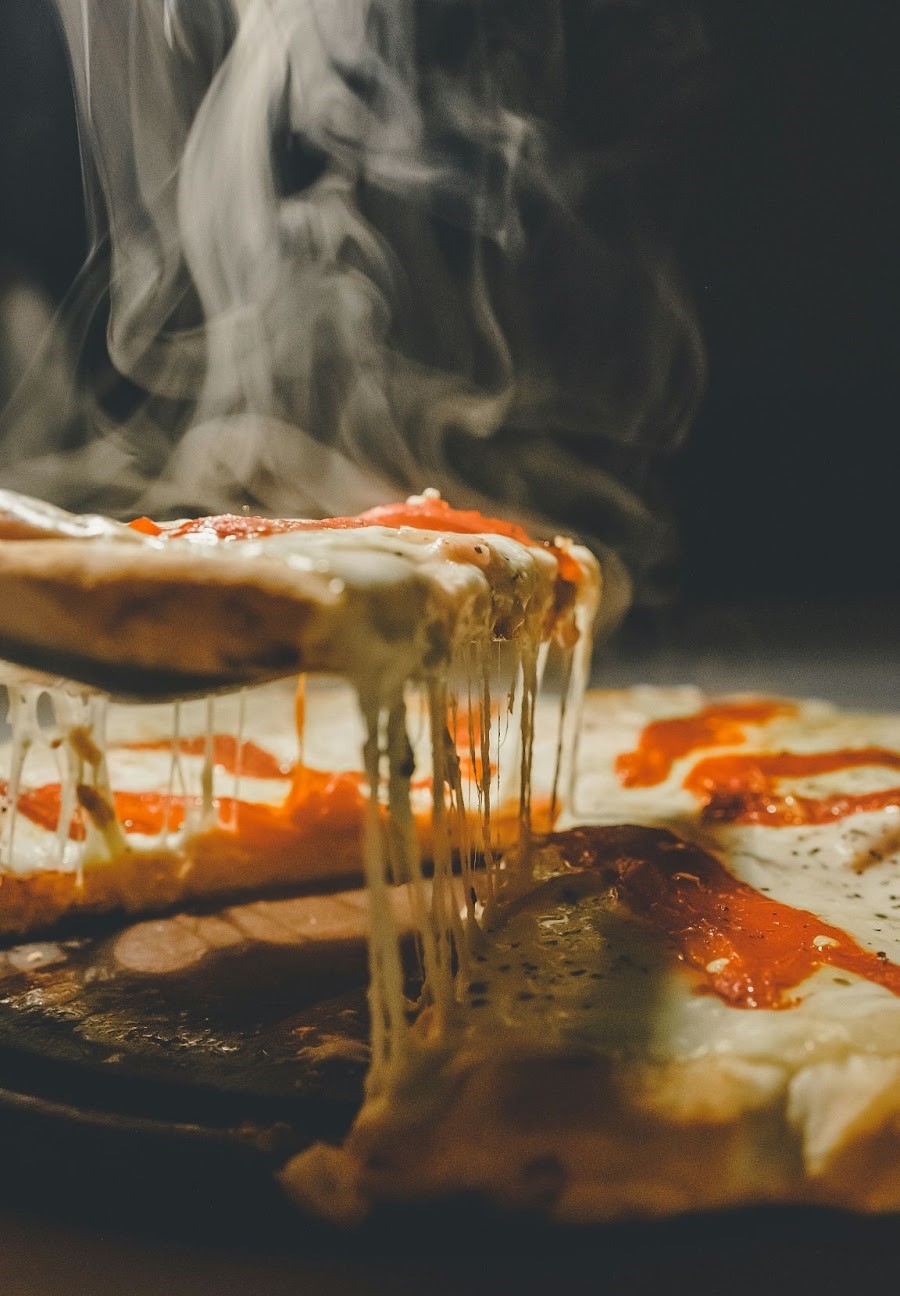 Steaming hot cheese pizza slice being pulled, with gooey melted mozzarella stretching long and steam rising.