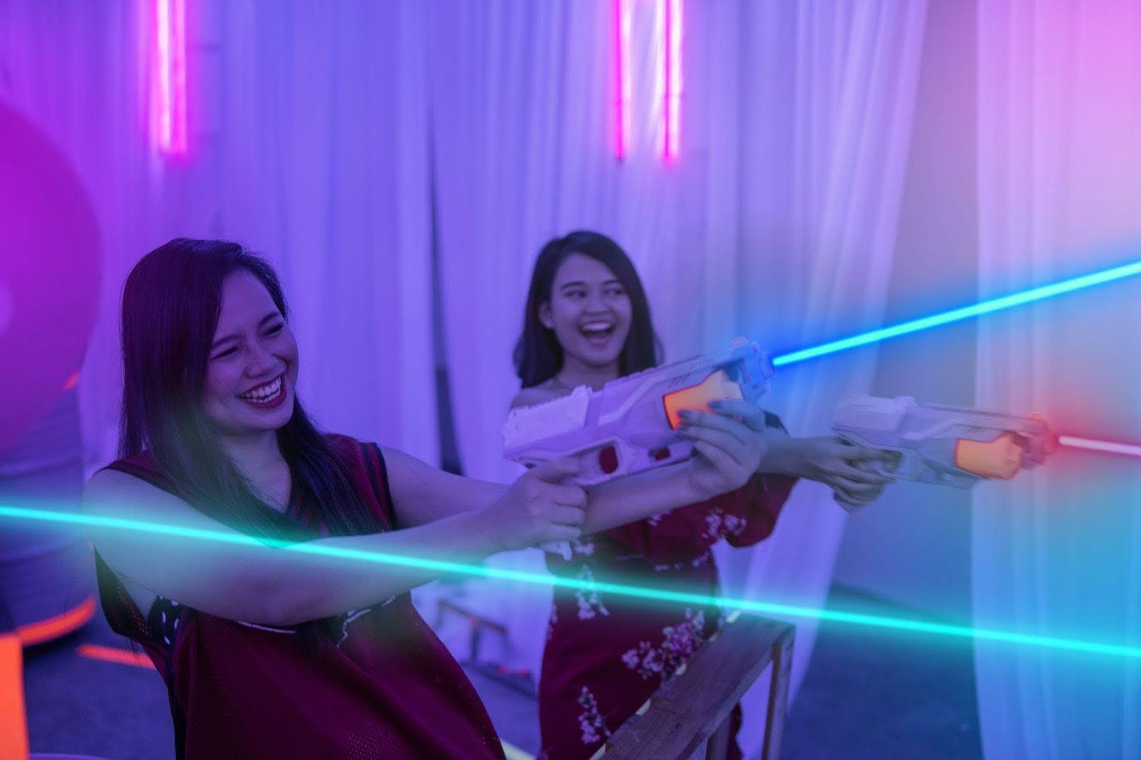 Two women having fun with laser guns in a colorful indoor setting