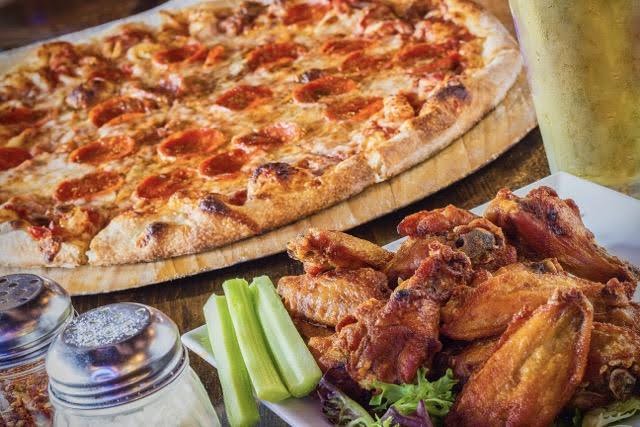 A pizza and chicken wings on a table beside a glass of beer creating a casual dining atmosphere