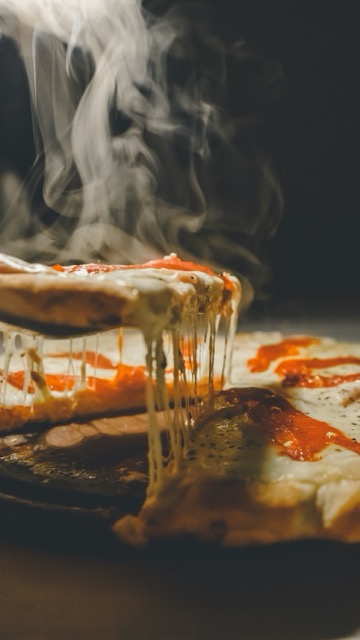 A slice of steaming hot pizza being lifted, showing melted cheese stretching from the tray.