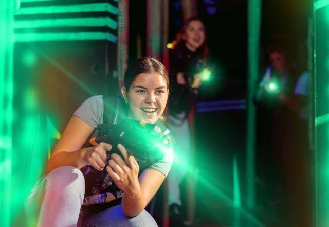 A woman with a gun poses in front of glowing green lights creating a dramatic and powerful atmosphere
