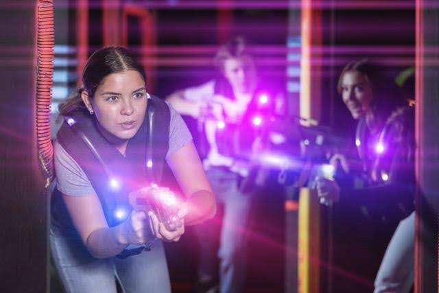 Three people playing laser tag indoors aiming glowing laser guns