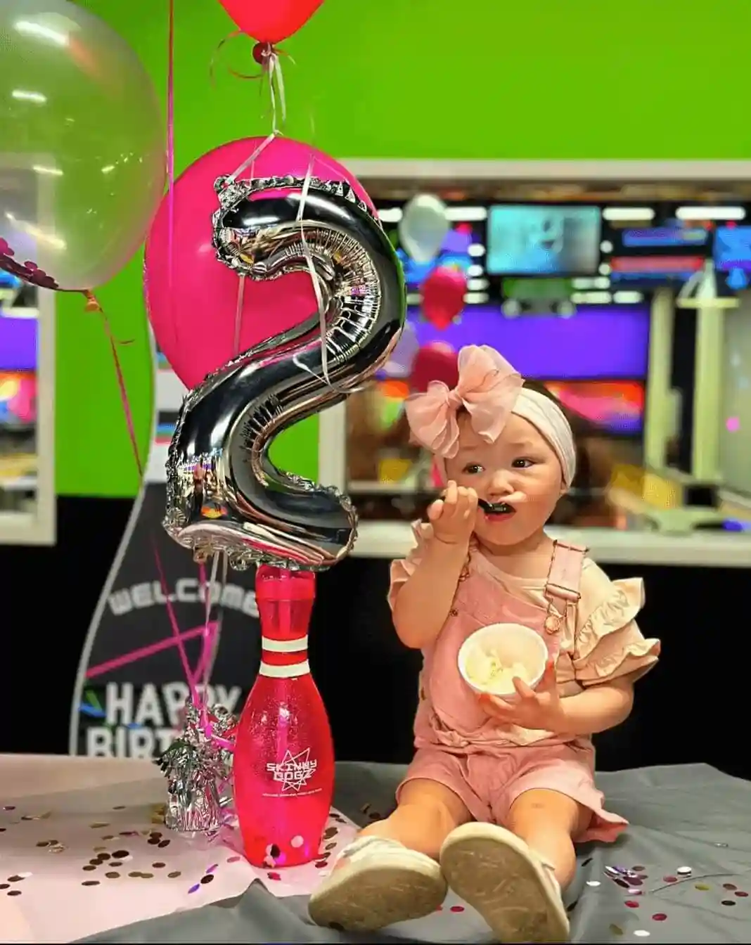  A baby girl sits on a table surrounded by colorful balloons and a birthday cake, celebrating her special day.