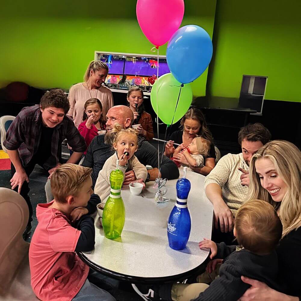 A group of people sitting around a table with colorful balloons, enjoying a festive atmosphere.