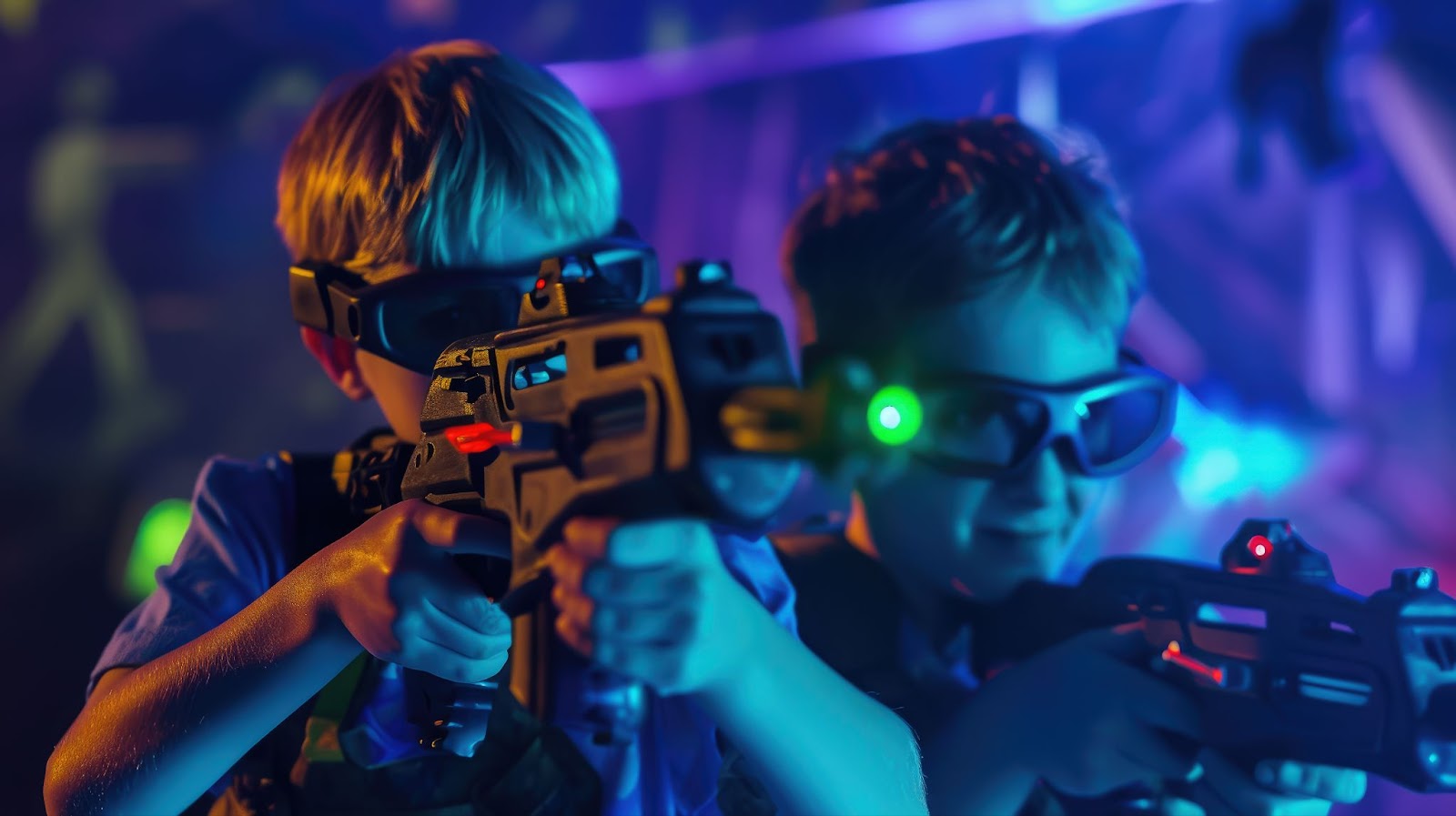 Two young boys holding toy guns in a dark room during a laser tag birthday party