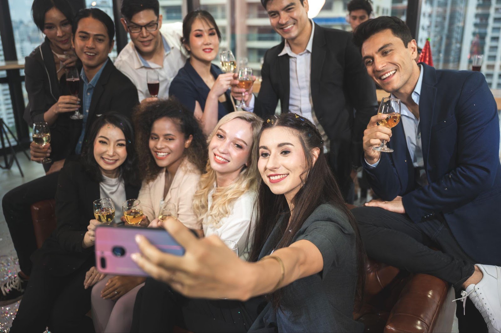 A diverse group of individuals smiling and taking a selfie with their cell phones
