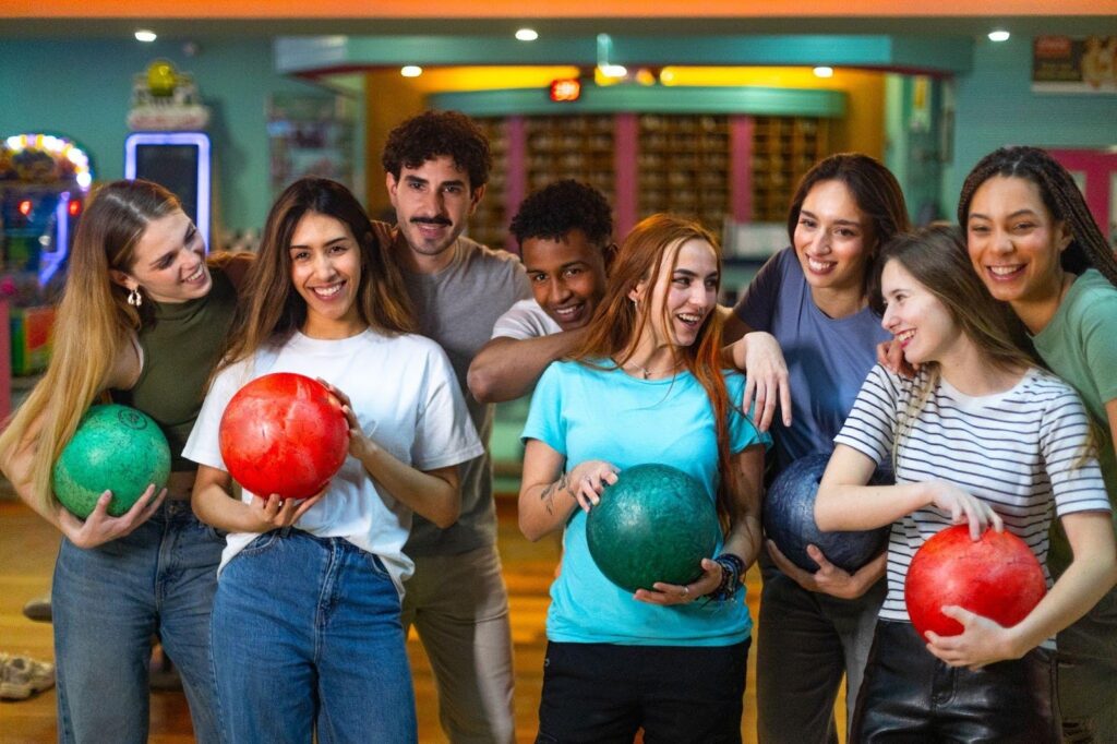 A group of smiling individuals holding colorful bowling balls ready to play a game together