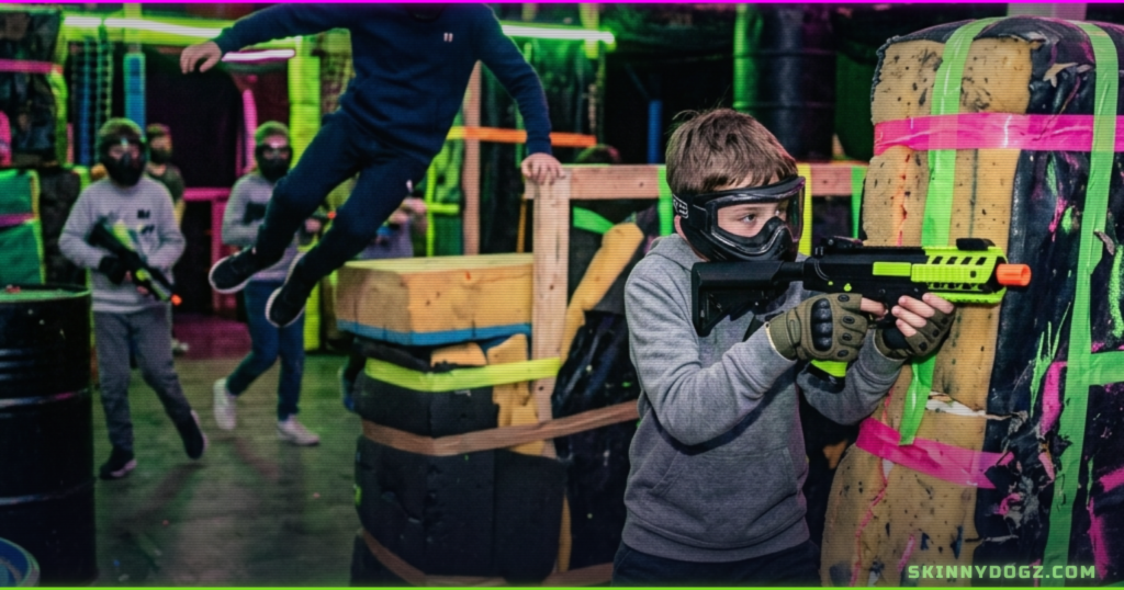 Players with gel blasters advancing through a neon-lit tactical arena, jumping and taking cover, indoor activity Ogden Utah